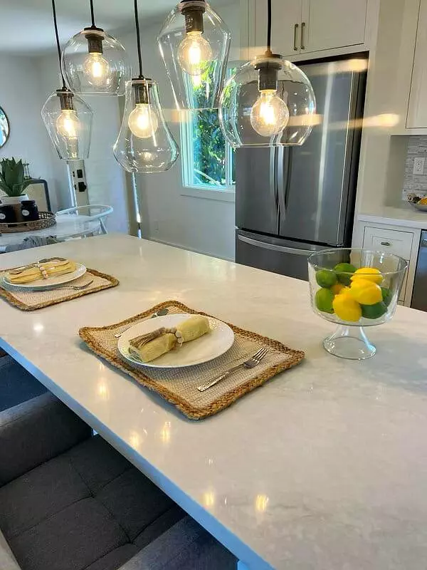 A kitchen with a white counter top and glass pendant lights.