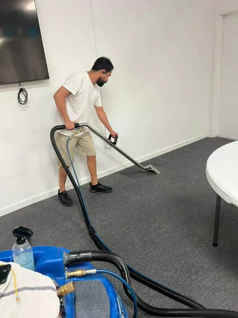 A man performing carpet cleaning with a vacuum.