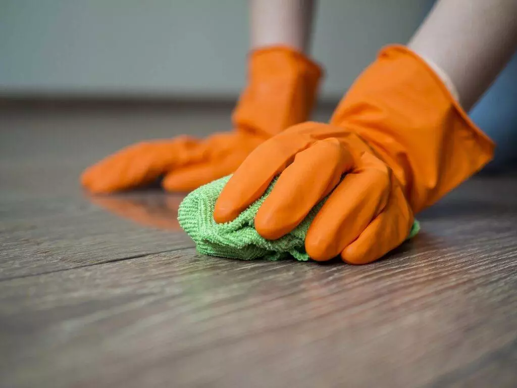 An expert cleaning services professional in San Jose wearing orange gloves while cleaning a wooden floor.