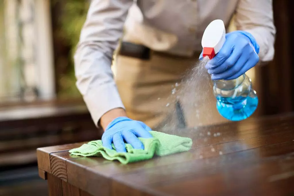 A woman expertly cleaning a wooden table in her living space with a bottle of cleaner.