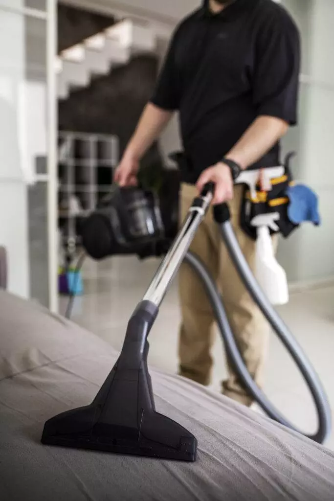 A man cleaning a bed with a vacuum in his living space.