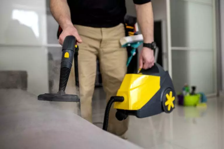 A man expertly cleaning a couch in his living space with a vacuum cleaner in San Jose.