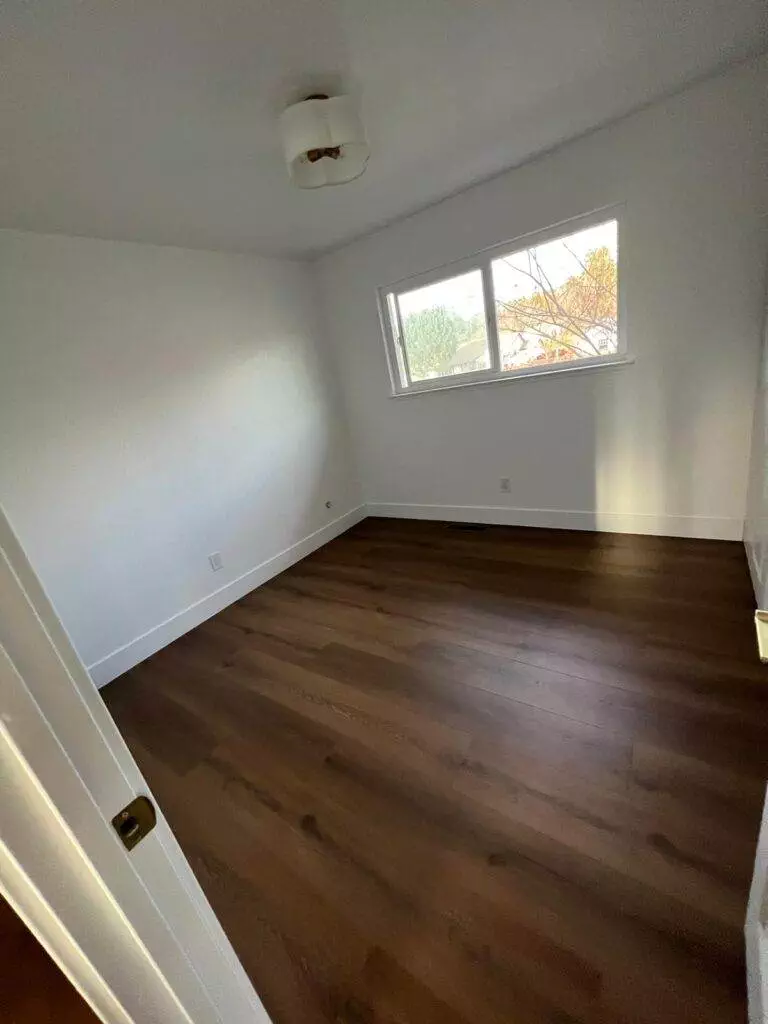 Empty room with hardwood floors, white walls, and a window letting in natural light.