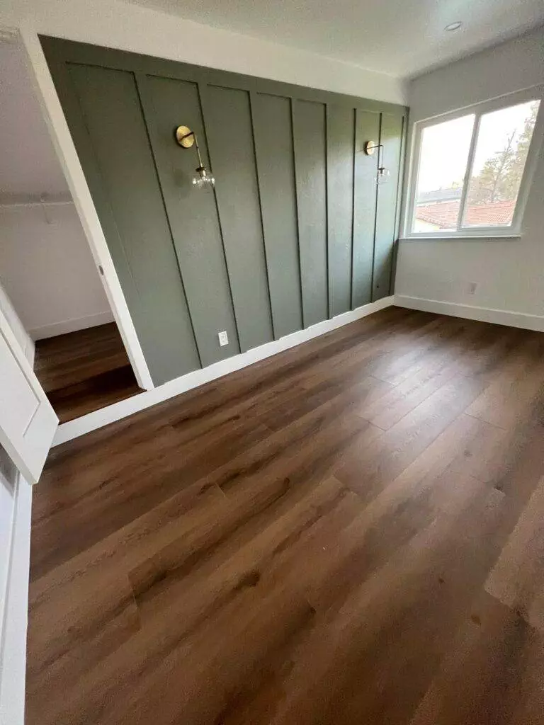 An empty room with herringbone wood floors, green paneled walls, and two wall-mounted lights.