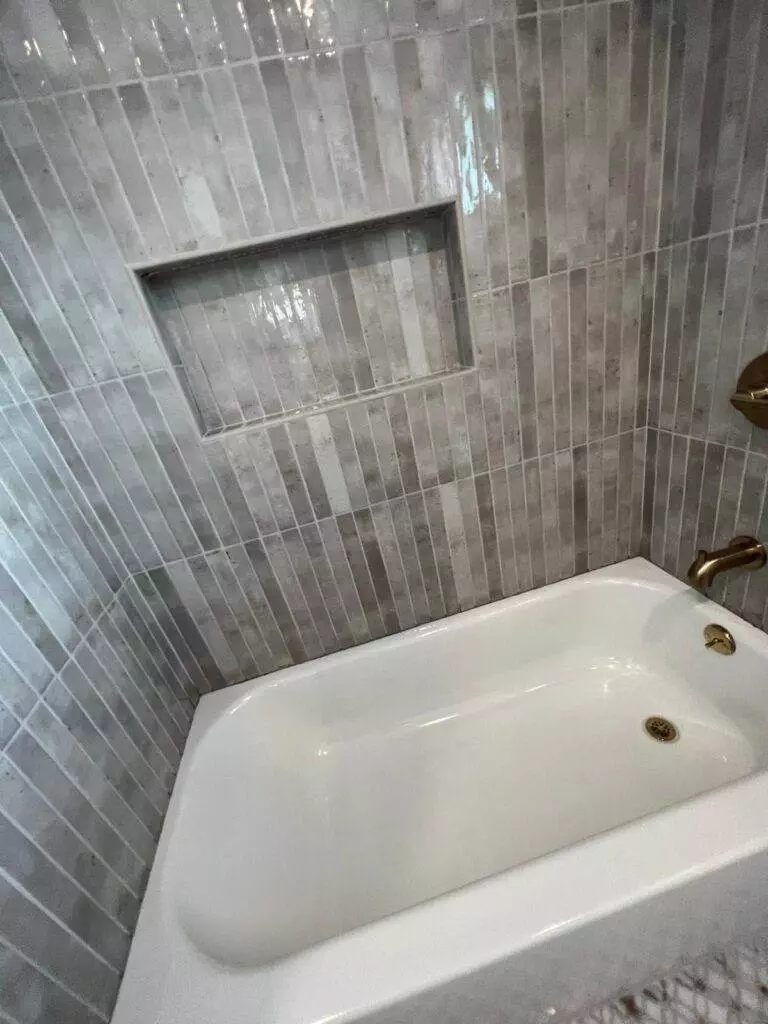 A corner bathtub with gold fixtures, surrounded by grey tiled walls with a built-in niche.