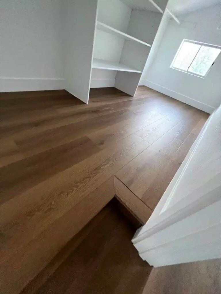 Bright, empty room with wooden flooring and built-in white shelves.