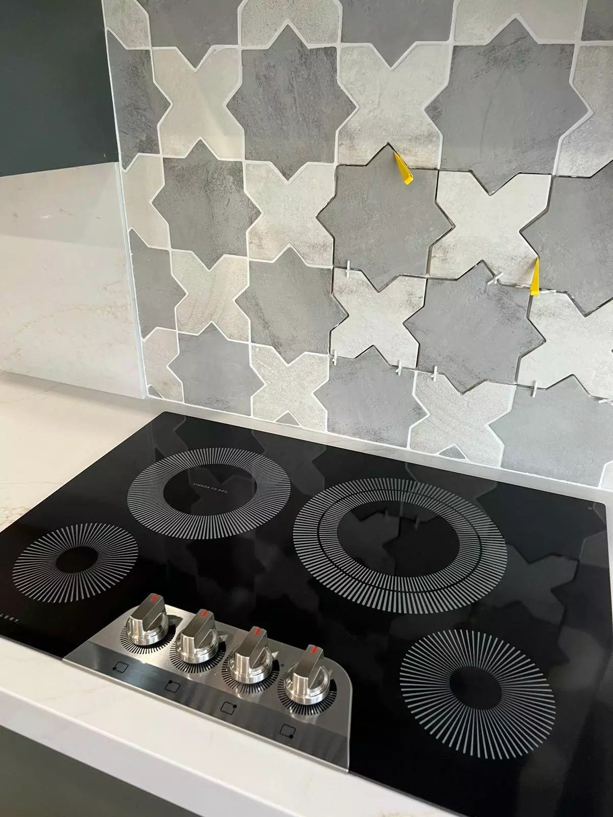 Electric stovetop with touch controls in a modern kitchen with hexagonal tile backsplash.
