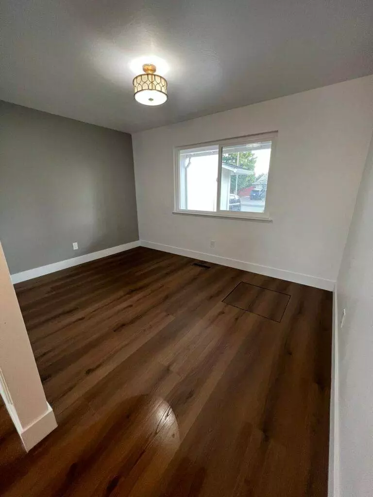 An empty room with grey walls, hardwood flooring, and a single window letting in natural light.