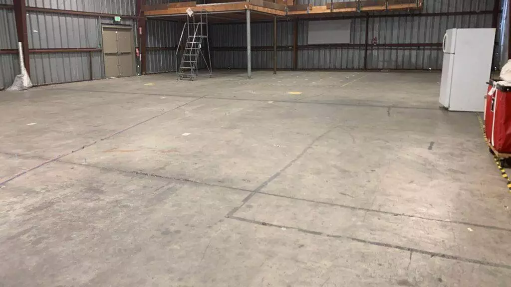 Large empty warehouse interior with concrete floor, metal walls, and a ladder on the right side undergoing transition.