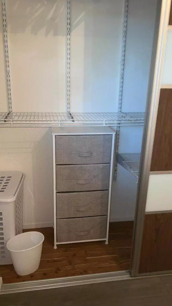 A small, gray fabric drawer unit inside a closet with white wire shelving, a mirrored door partially visible on the right, exemplifies unparalleled cleanliness.