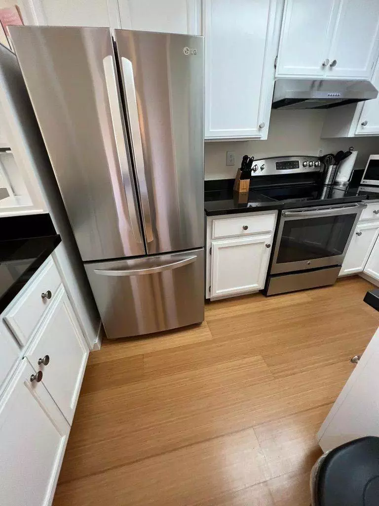A modern kitchen in Cupertino with stainless steel appliances including a fridge, oven, and microwave, set against white cabinetry and hardwood floors.