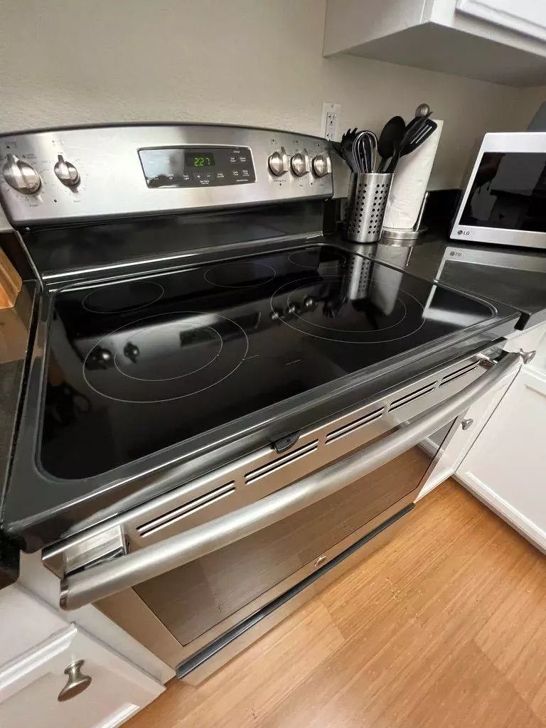A modern kitchen featuring a stainless steel electric stove with a sleek black cooktop, utensil holder on the left, and a microwave in the background ensures satisfied guests.
