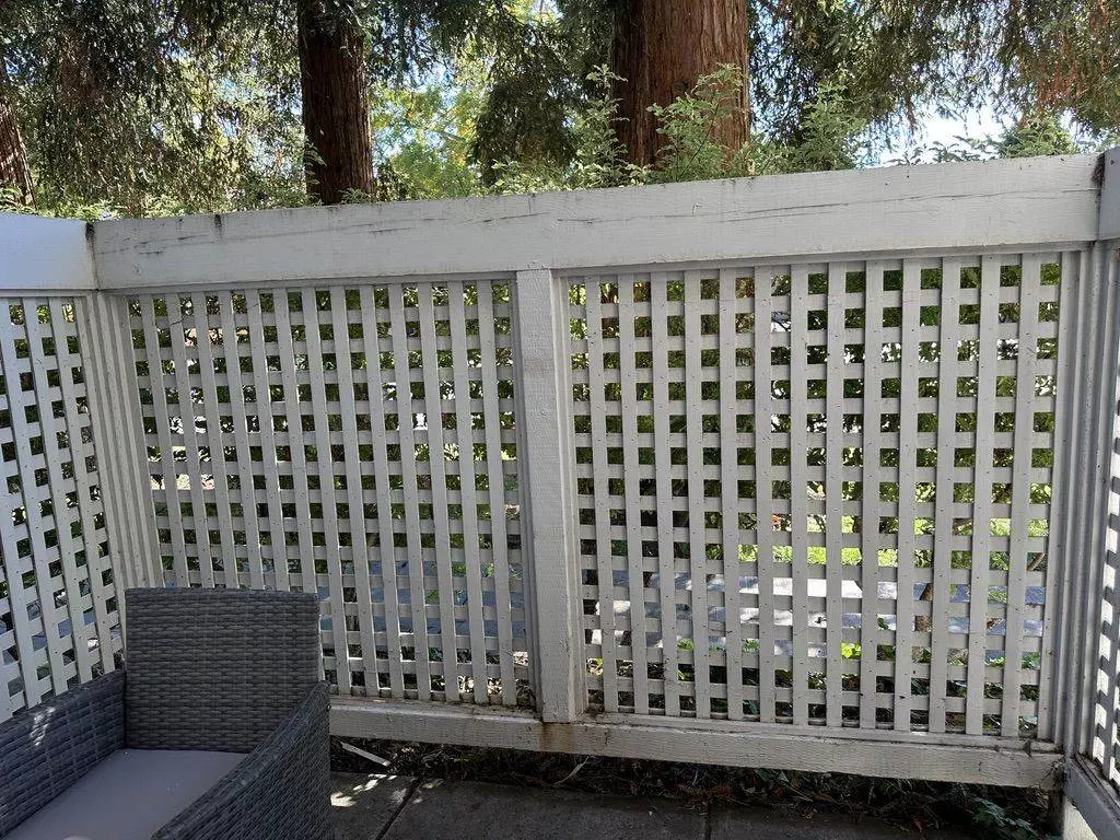 White lattice fence bordered by trees with a single grey armchair in front, set in a sunny outdoor area, meticulously maintained with Master Clean Service.