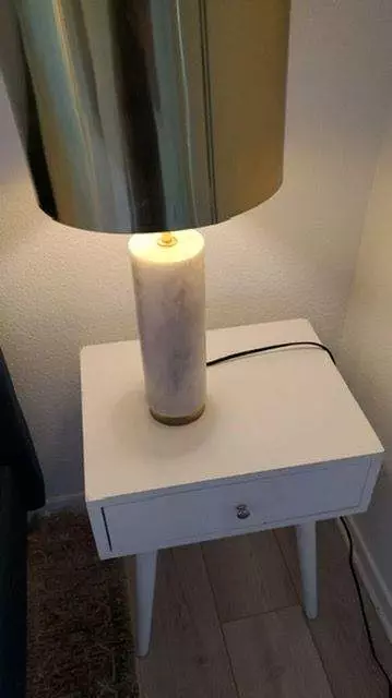 A small white nightstand with a single drawer and slender legs, holding a cylindrical marble lamp, sits beside a silver lampshade in a corner, exemplifying the meticulous attention to detail provided by Master Clean