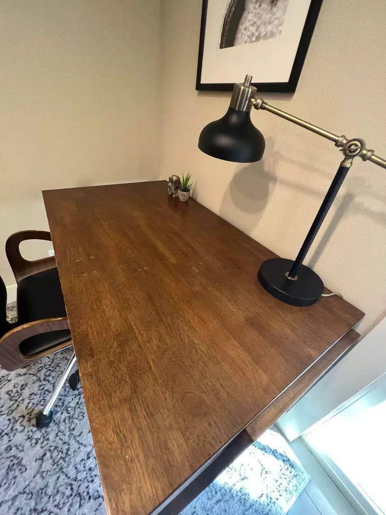 A well-lit wooden desk with a metal lamp on the right, a small plant at the back, and a brown chair tucked under it, positioned in a cozy room corner after a deep cleaning.