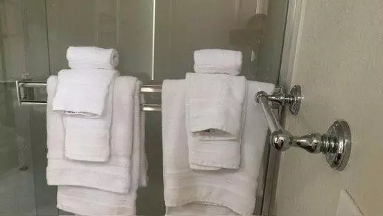 Two stacks of immaculate white towels on metal racks beside a glass shower door in a bathroom.