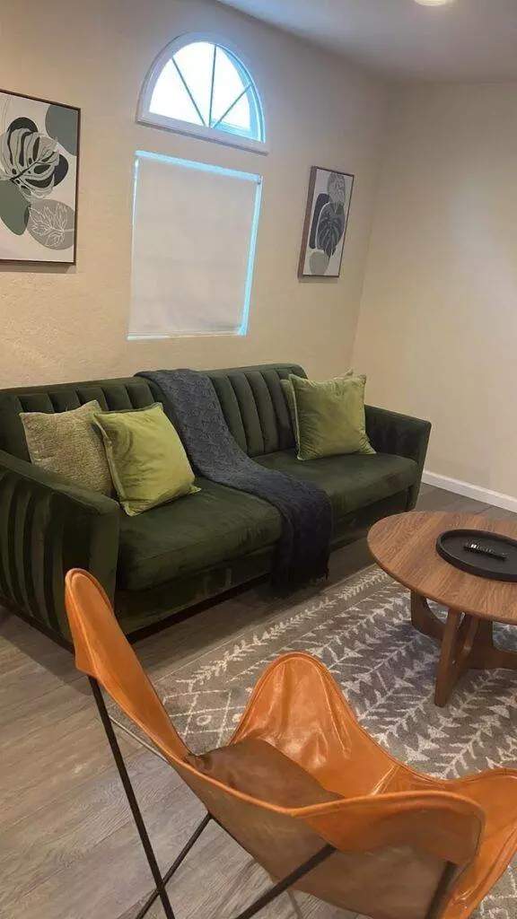 A cozy living room featuring a green sofa with lime cushions serviced by Master Clean Service, a tan leather chair, a round coffee table, and decorative plant prints on the wall.