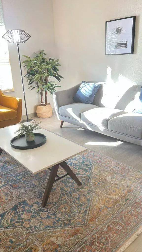 Modern living room with natural light, featuring a grey sofa, mustard armchair, white coffee table, ornate rug, and an indoor plant maintained by Fremont Deep Cleaning.