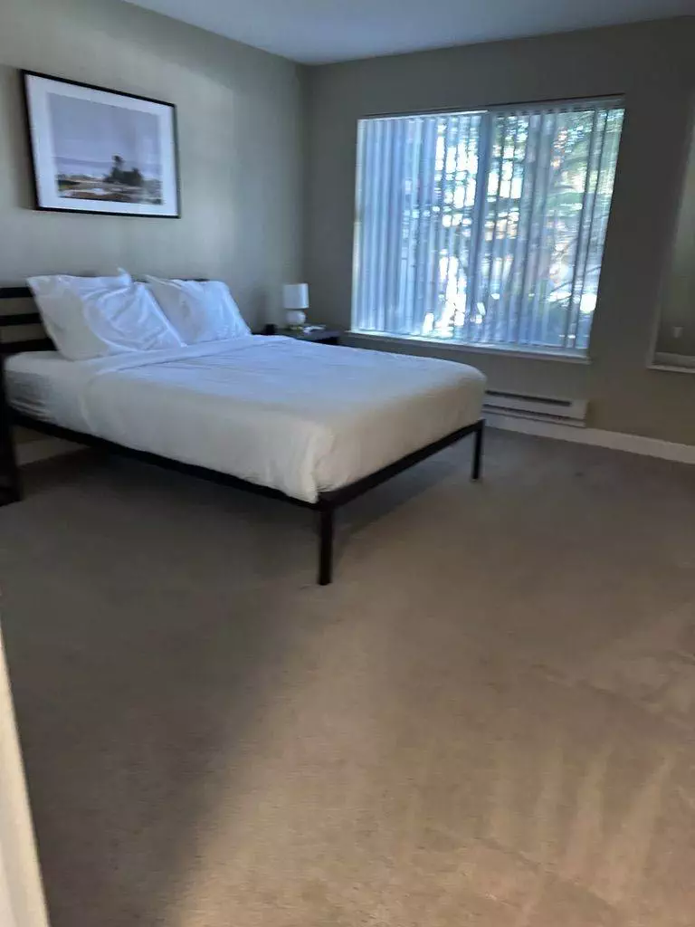A tidy bedroom with a minimalist design, ideal for minimizing stress during your move, featuring a single bed, a large window, and a framed picture above the bed.
