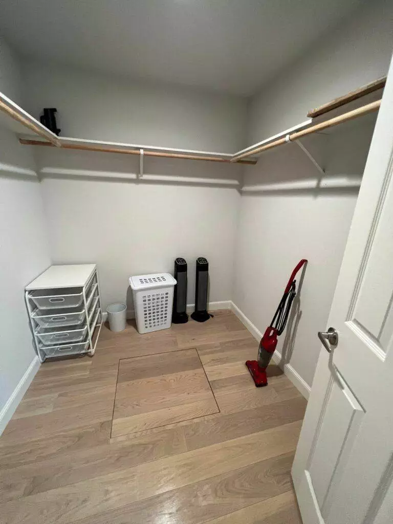 A small, empty closet with wooden floors, white walls, and built-in shelves includes a vacuum cleaner from Master Clean Service, storage drawers, and two air purifiers.