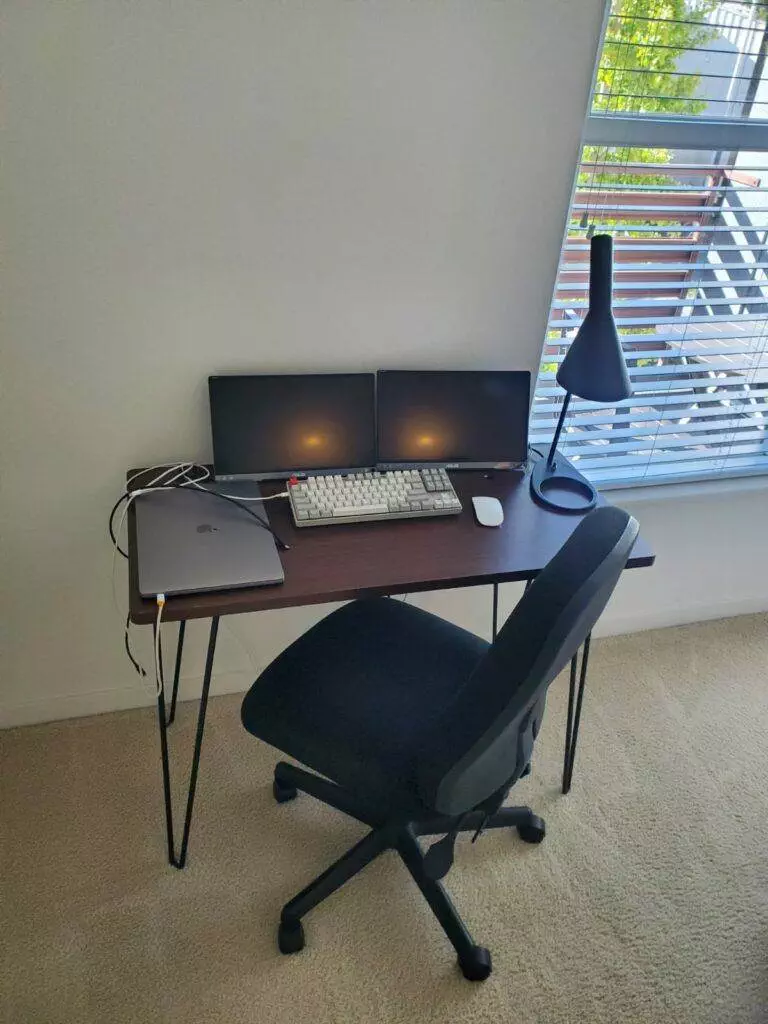 A professional home office setup in Union City with a desk, two monitors, a laptop, a mechanical keyboard, and an ergonomic chair near a window with blinds.