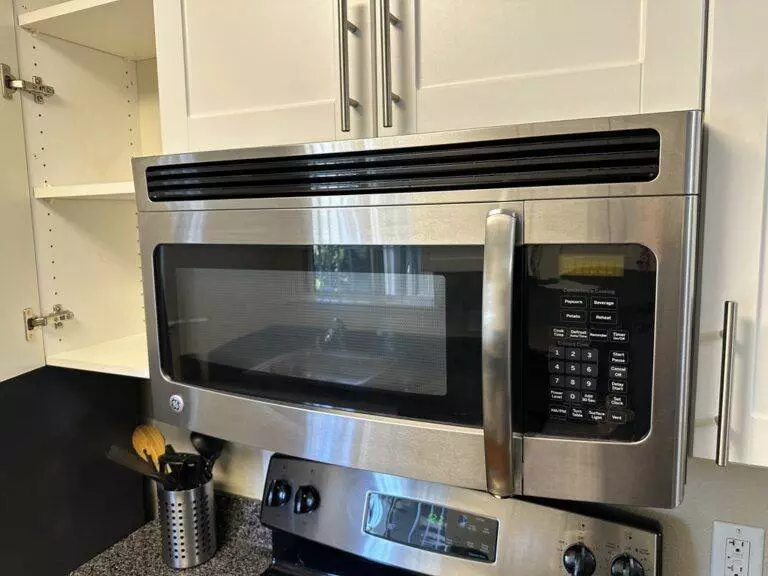 Stainless steel microwave oven mounted above a stove in a kitchen with white cabinets, featuring unparalleled cleanliness.