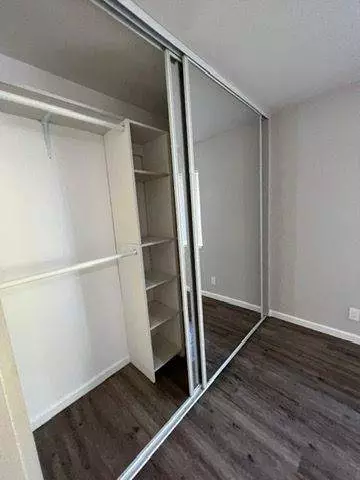 An open mirrored sliding closet door revealing built-in shelves and hanging rods in a room with gray flooring, freshly maintained by Master Clean Service.