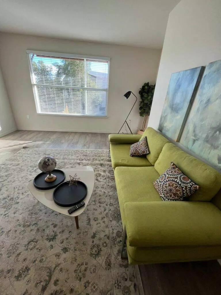 Modern living room with a green sofa expertly maintained by Santa Clara Upholstery Cleaning, featuring a round coffee table, and large window with blinds. Decor includes a plant, cushions, and a floor