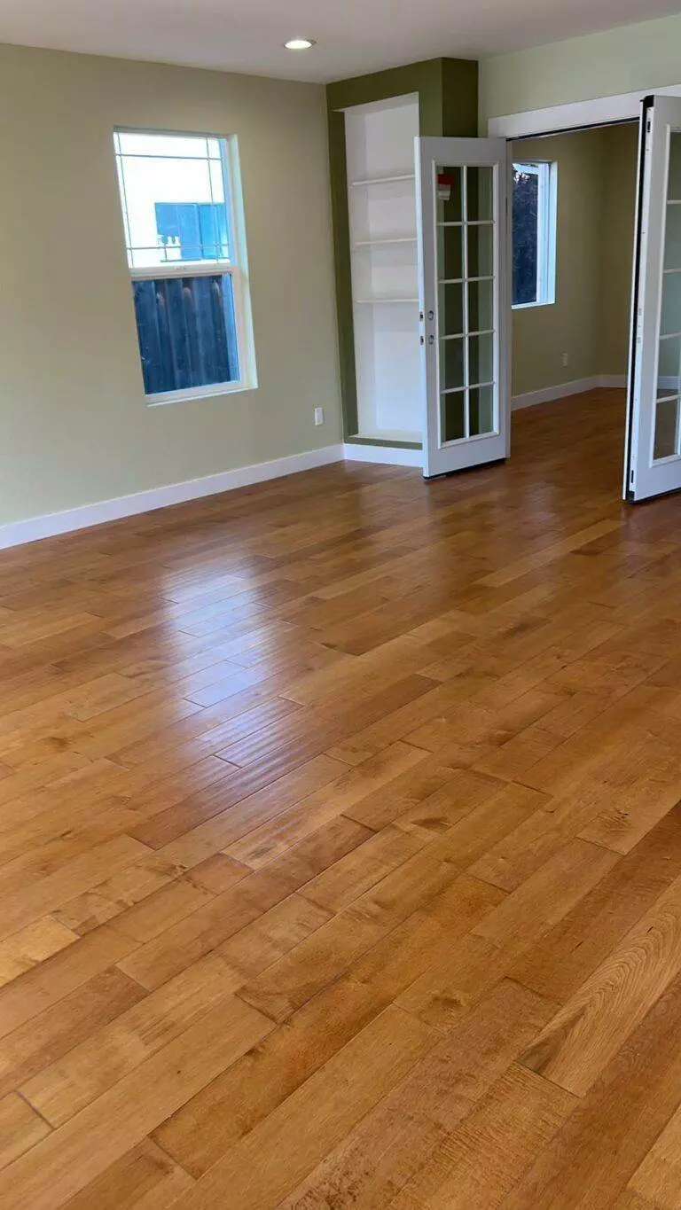 Empty room with wooden flooring, white walls, and glass-paneled doors leading to adjacent rooms, all featuring a flawless finish.
