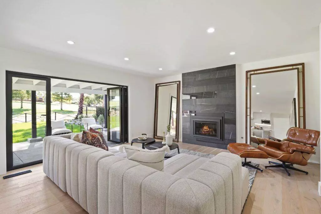 Modern living room with a gray sofa, leather chair, fireplace, and sliding glass doors opening to a garden, featured in a construction portfolio.