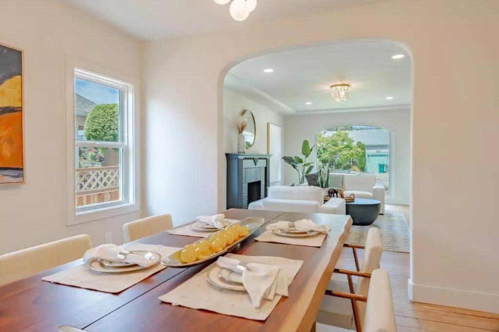 Modern dining room with a wooden table set for six, leading to an archway with a view into a living area. Bright, natural light fills the space, highlighting the post-construction finish.