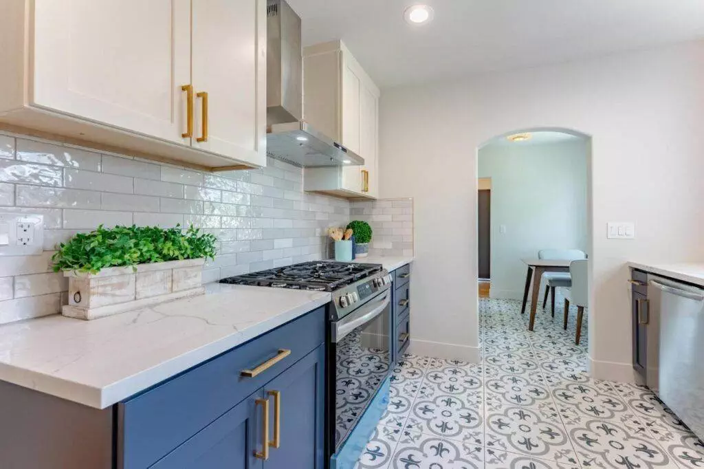 Modern kitchen with blue cabinetry, white countertops, subway tile backsplash, and patterned floor tiles, leading to a dining area—featured in our post-construction portfolio.