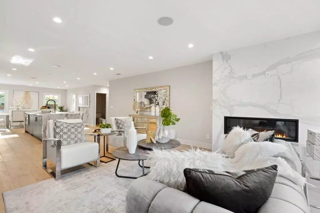 Modern living room with a sectional sofa, glass coffee table, and a fireplace, connecting to an open-plan kitchen. Bright and airy space with contemporary decor and suitable for inclusion in a construction portfolio.