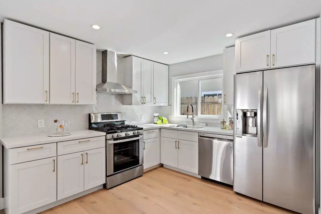 Modern kitchen with white cabinets, stainless steel appliances, and a hardwood floor, featured in our construction portfolio.