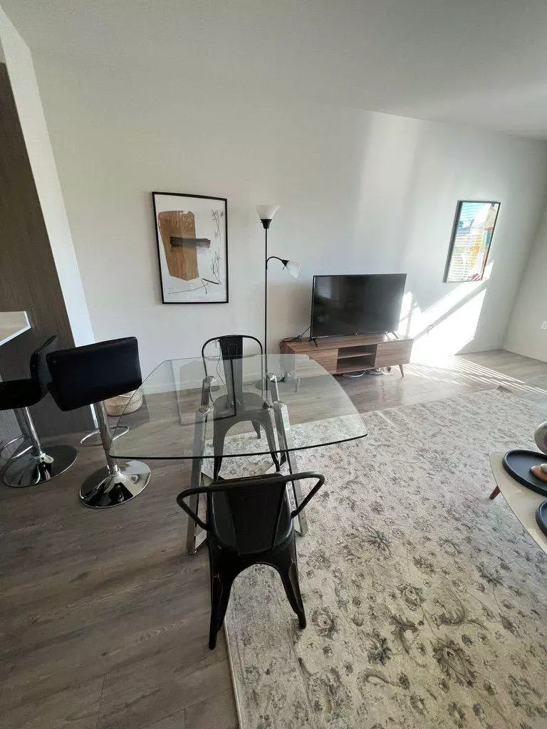 A modern dining room with a glass table, black chairs, and a TV in a bright, minimalist apartment suitable for short-term rentals.