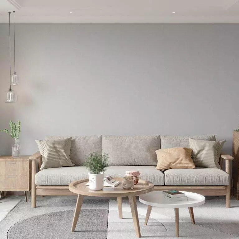 A modern living room with a beige sofa, two round coffee tables, and decorative plants. The walls are light grey and minimalistic. Hanging lights and matching cushions accentuate the decor, maintaining a fresh look thanks to professional upholstery cleaning services in Campbell.