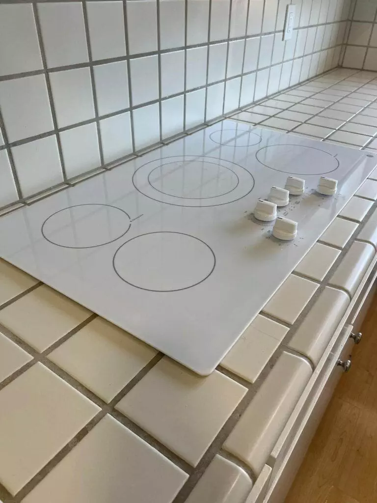 A white electric stovetop with four burners and four control knobs on a tiled countertop.