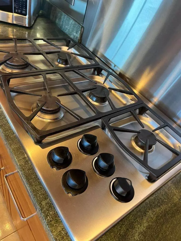 A stainless steel gas stove with five burners and four control knobs is installed on a kitchen countertop.