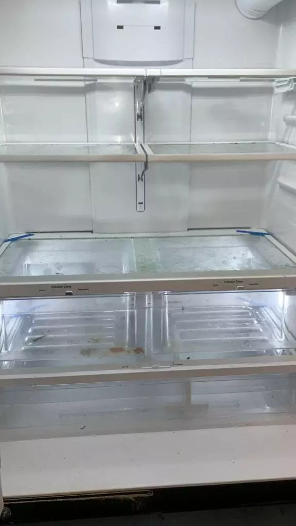 An empty refrigerator with four shelves, some stains and dirt are visible at the bottom.