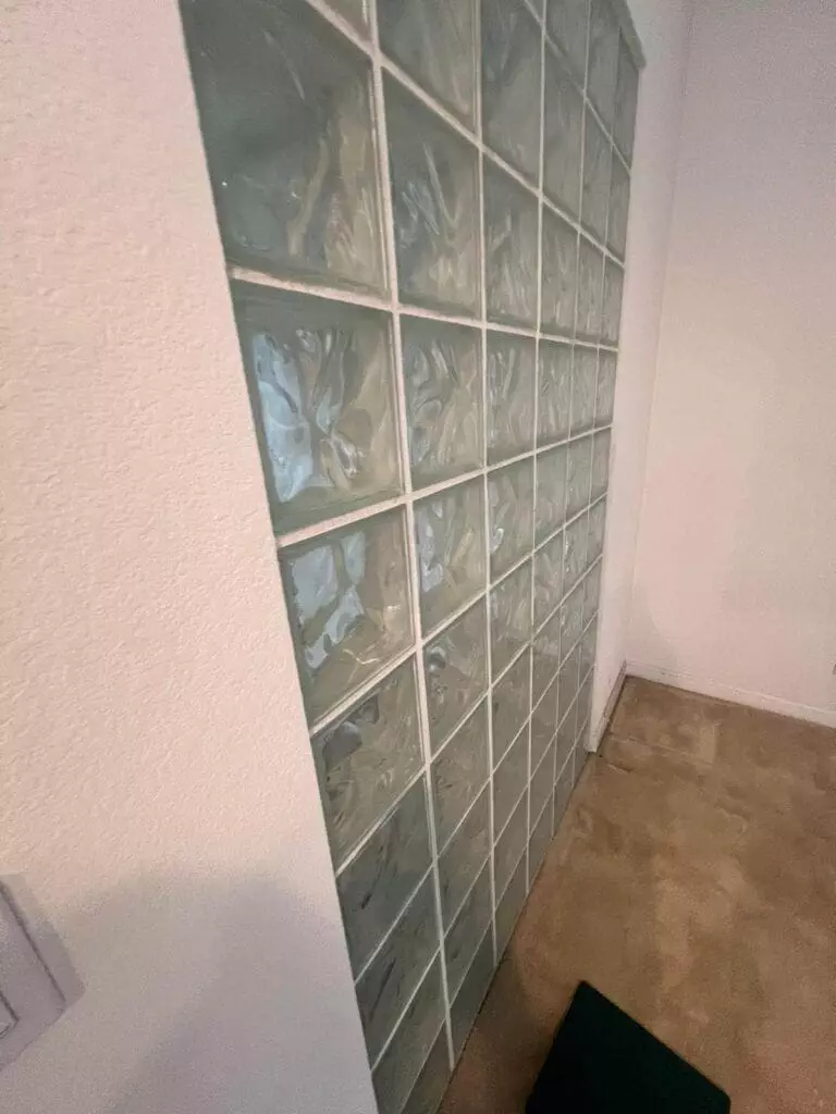 A wall made of translucent glass blocks next to a white painted wall and beige carpet flooring.