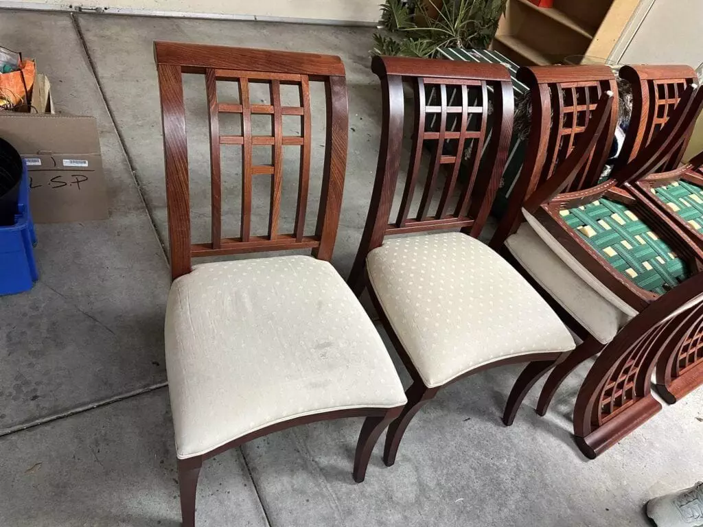 Two wooden chairs with light-colored upholstered seats are in the front, and several more chairs with green webbing on the seats are arranged behind them. Various items are in the background.