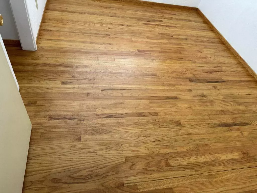 A room with a wooden hardwood floor and white walls. The door is slightly open, leading into a visible corridor.