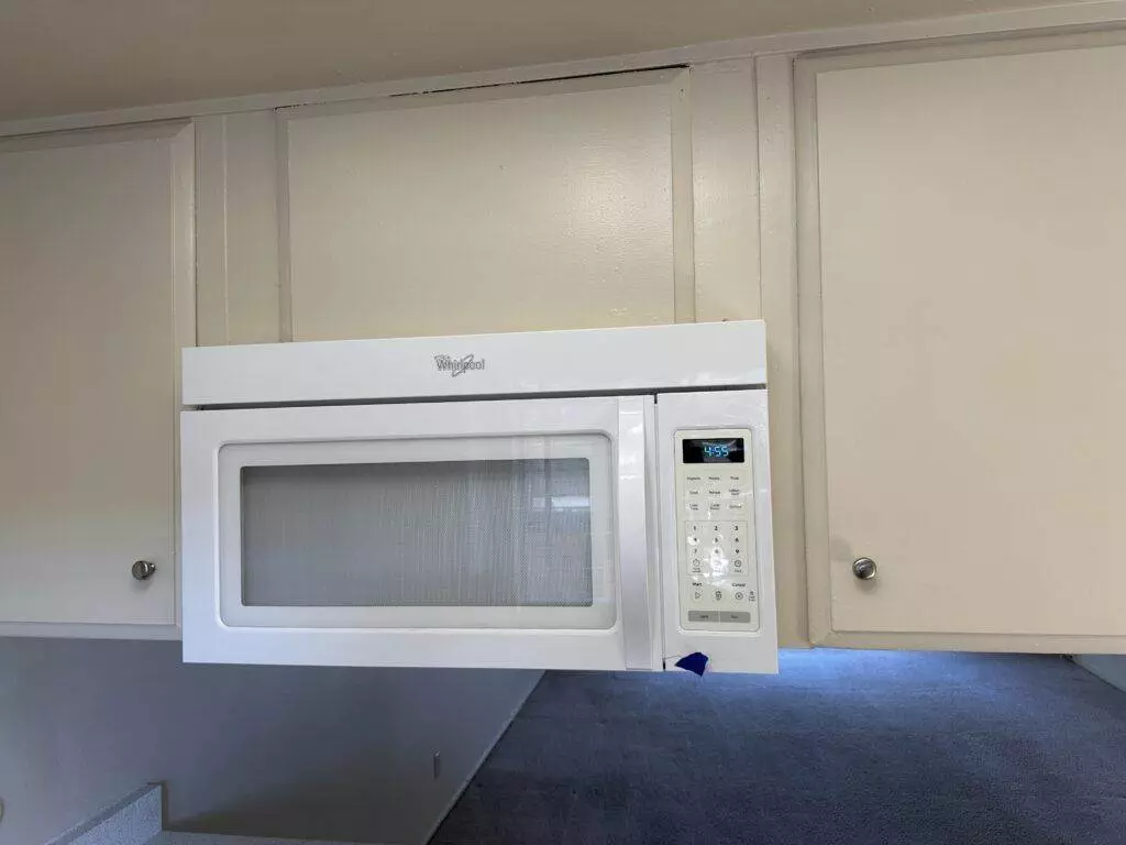 A white microwave is mounted under kitchen cabinets above a stove. The door and control panel are visible.