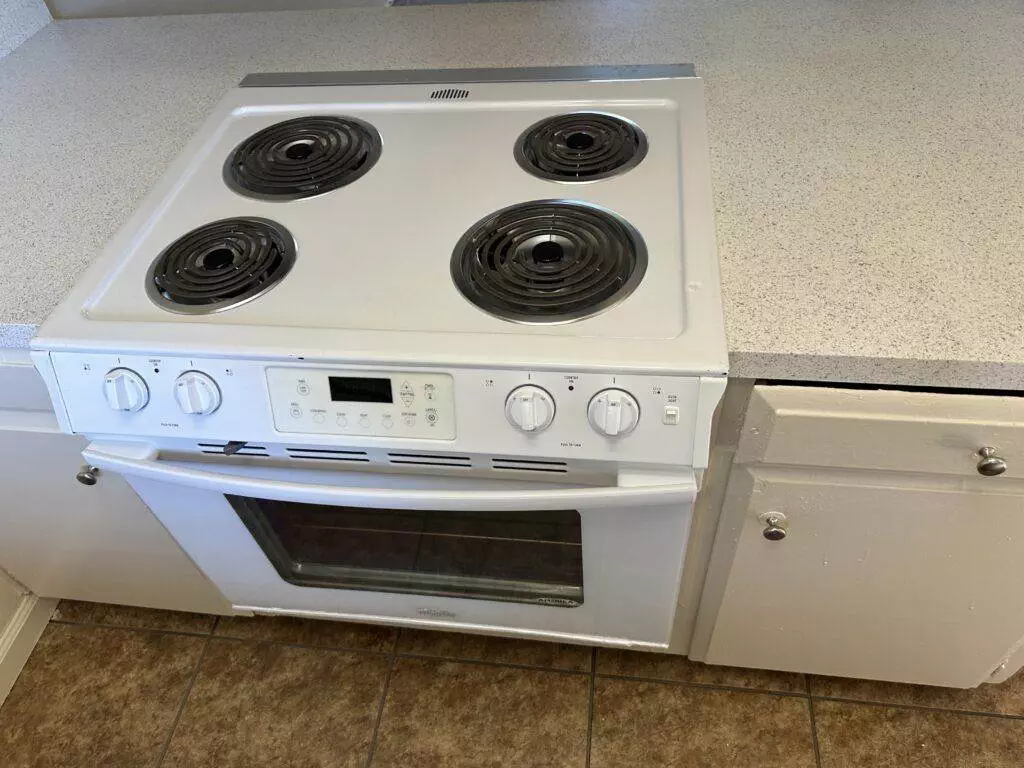 A white electric stove with four coil burners and an oven below, situated between two white cabinets on a tiled kitchen floor.